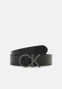 Cintura in pelle nera con motivo a diamante, dotata di una fibbia in metallo nero opaco impressa con "CK". Il design è sottile ed elegante.
