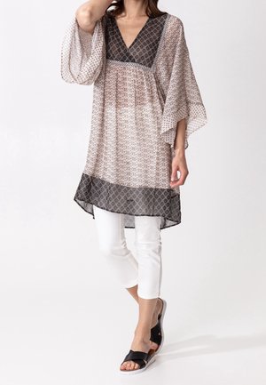 Letvægtsmønstret tunika med sort V-halsudskæring, flydende ærmer og sort kant. Kombineret med hvide capris og sorte sandaler.