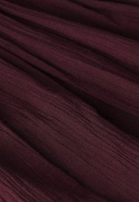 Deep burgundy fabric with soft, narrow vertical pleats creating textured, flowing folds.