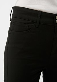 Jeans en denim noir avec un design classique à cinq poches, présentant une texture lisse, des passants de ceinture et des accents de boutons argentés.