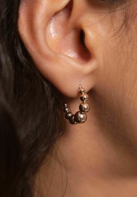 Metallohrringe mit runden Perlen in verschiedenen Größen, die ein geschwungenes Design und eine glänzende Oberfläche aufweisen und am Ohr getragen werden.