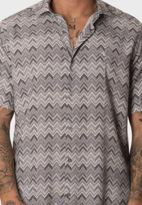 Camisa de botones de manga corta con un patrón de zigzag en gris, negro y blanco, hecha de un tejido suave y con un corte relajado.