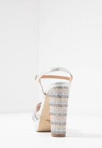 Stříbrné sandály na vysokém podpatku s lesklým svrškem, páskem kolem kotníku a texturovanou platformou s alternujícími řadami zlatých a stříbrných rhinestones.