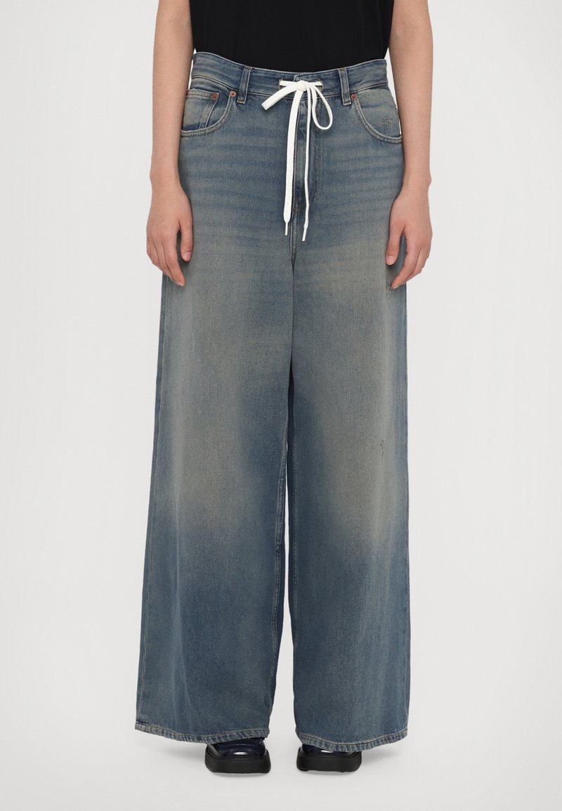 Jeans blue chiaro a gamba larga realizzati in denim, con vita regolabile e sfumature sottili. Due tasche frontali con dettagli di cucitura in evidenza.