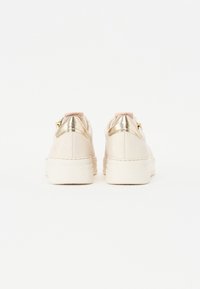 Lys beige sneakers med en glat finish, gyldne detaljer ved hælen og en struktureret gummisål. Bagfra ses en polstret krave.