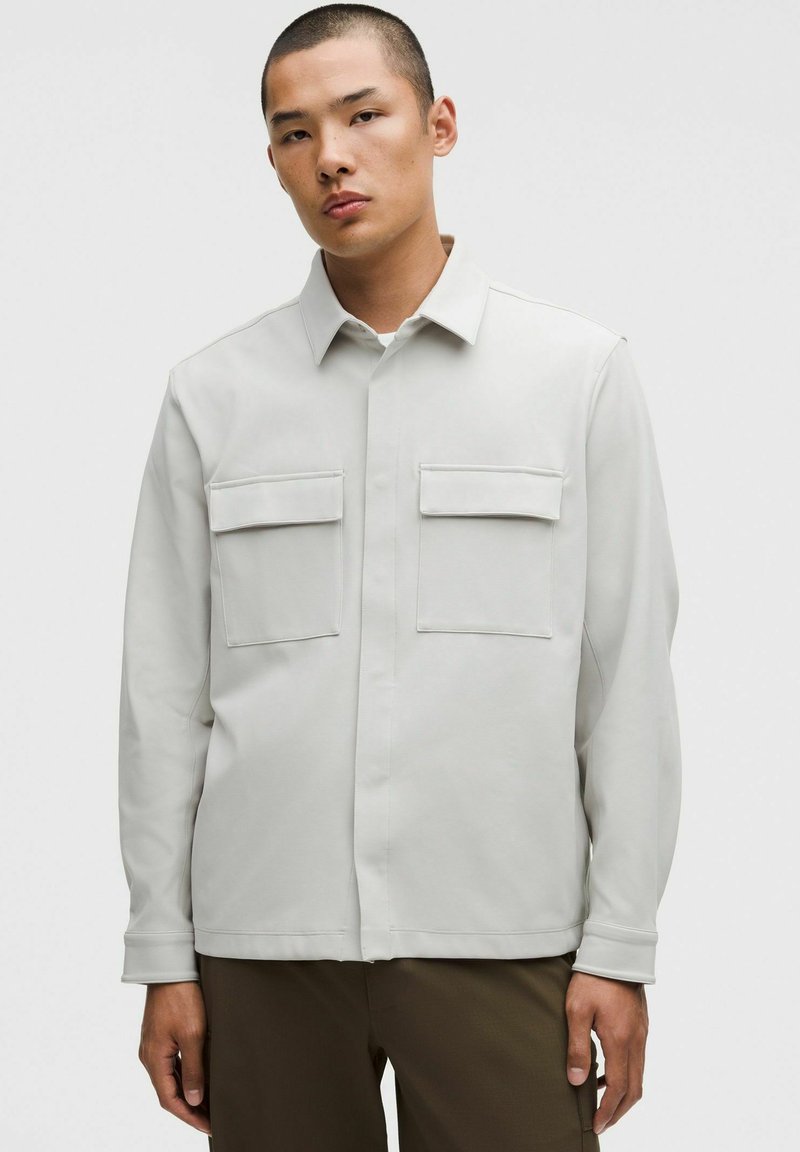 Hele halli pika varrukaga särk kraega ja kahe rinnataskuga. Sujuv tekstuur ja minimalistlik disain, millel on tikitud aktsendid.