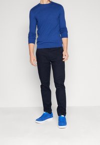 Maglione lavorato a maglia blu a maniche lunghe abbinato a pantaloni blu scuro e sneakers blu. Il maglione ha un collo rotondo; l'outfit è casual.
