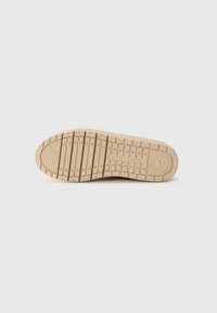 Beiger Sneaker-Sohle mit strukturierten Grip-Mustern, abgerundetem Zeh und Markendetails; flaches Design mit tiefer Einsenkung für Traktion.