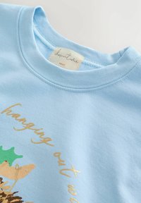 Lyseblå crewneck sweatshirt med en syet halsudskæring, delvis tekst "hanging out" i guld og et stofmærke med teksten "downtime NEXT."