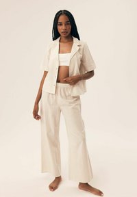 Jasnoszary, pasek w dwóch częściach, składający się z koszuli z krótkim rękawem z guzikami oraz spodni z szerokimi nogawkami, wykonany z gładkiego materiału.