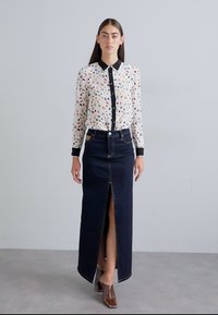 Biela košeľa s gombíkmi a farebnými vzormi, v kombinácii s tmavo modrou maxi sukňou z denimu s predným rozparkom a kontrastným prešívaním.