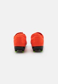 Scarpe da calcio rosse con tomaia texturizzata, dotate di suola nera e tacchetti verdi. Il design include dettagli di cucitura sul tallone.