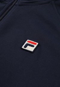 Marine hoodie med broderet logo i rød, hvid og blå. Materiale: blød bomuldsblanding. Design: lynlås foran med en tekstureret overflade.