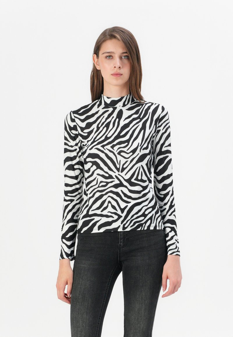 T-shirt à manches longues dans un motif zèbre noir et blanc, avec un col montant et un tissu extensible ; associé à un jean noir.
