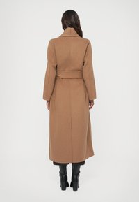 Long manteau en laine marron avec une taille ceinturée, un col à revers et des manches longues ; texture lisse ; tombe au milieu du mollet.