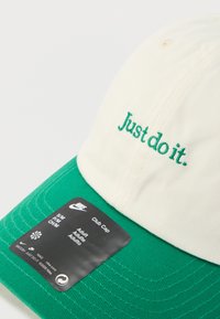 Fehér korona és zöld napellenzővel ellátott sapka. Zöld hímzéssel díszített "Just do it." felirat. Fekete címke méretezési és márkajelzési információkkal.