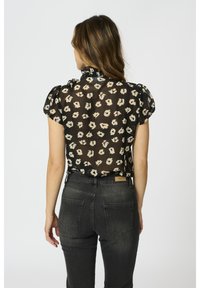 Svart genomskinlig blus med krämfärgad blommönster, puffärmar, volangkrage, kombinerad med mörk denimjeans med bakfickor och varumärkeslogotyp.