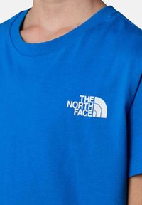 T-shirt in cotone blu con scollo rotondo, caratterizzato da un logo bianco di "The North Face" nell'area del petto sinistro. Tessuto morbido, maniche corte.