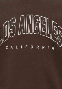 Tissu marron avec texte blanc « LOS ANGELES » en grandes lettres et « CALIFORNIA » en lettres plus petites en dessous.