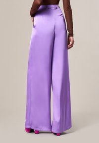 Pantaloni ampi in satin di un leggero colore lavanda, con una texture morbida, vita alta e tasche laterali, abbinati a scarpe con dettagli rosa a contrasto.