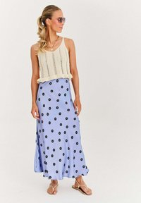 Pletený krémový top s volánovým lemom, kombinovaný s svetlo modrou maxi sukňou zdobenou čiernymi kvetinovými vzormi a béžovými sandálmi.