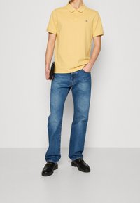 Gul polo skjorta med krage, i kombination med blå raka jeans. Svarta skor med subtila detaljer. Enkel design, jämn textur.