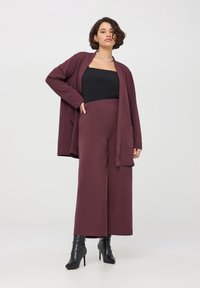 Bordo cardigan z kieszeniami, czarny top bez ramiączek i szerokie bordowe spodnie. Noszony z czarnymi botkami na wysokim obcasie.