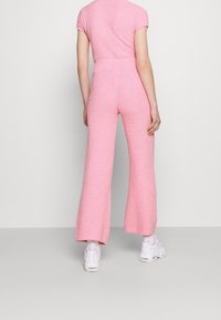 Roze gebreide jumpsuit met korte mouwen, wijde broekspijpen, textuurstof en een relaxte pasvorm. Gemaakt in combinatie met witte sneakers.