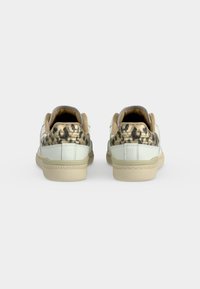 Ζευγάρι λευκά sneakers χαμηλού ύψους με μπεζ σόλες και λεπτομέρεια λεοπάρ στο πίσω μέρος, εμφανίζονται από πίσω σε απλό φόντο.