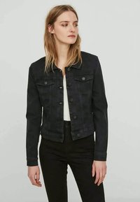Svart denimjakke med knappestengning, to brystlommer og en tettsittende design. Har klassisk krage og lange ermer med knappede mansjetter.