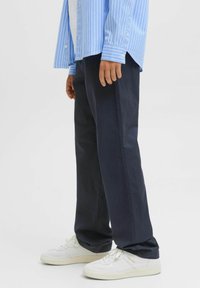 Marineblauwe katoenen broek met een rechte snit, gecombineerd met witte sneakers. Zichtbare verticale strepen op een blauwe overhemden.