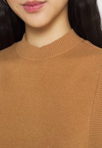 Brązowy sweter dziany z prążkowanym półgolfem. Tkanina jest gładka o lekko błyszczącej fakturze, z prążkowanymi wstawkami po bokach.