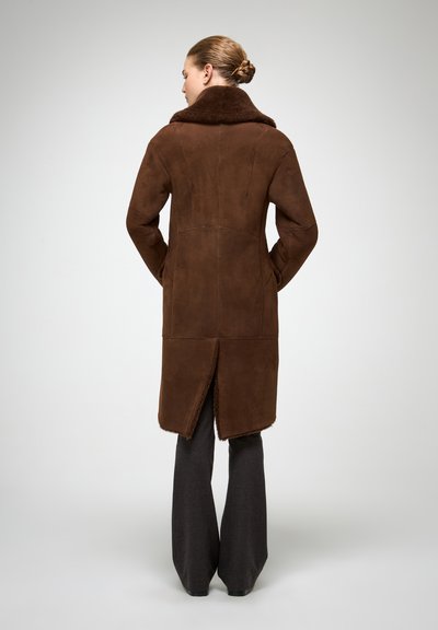 Pruun seemismantel kunstkarusnahast kraega, sirge lõike ja tagaküljel kõrge lõhikuga. Sobitatud tumehallide laiade pükstega.