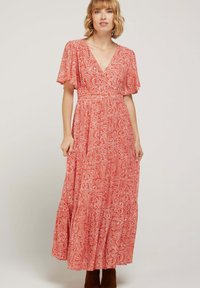 Robe maxi rouge avec un motif paisley blanc, manches courtes volantées, décolleté en V et jupe à volants. Le tissu est léger avec une texture douce.