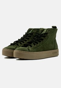 Zapatillas altas de ante verde con cordones negros, ojales dorados, suela de goma texturizada y una lengüeta en la parte trasera para ponerlas y quitarlas fácilmente.