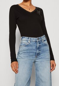 Body a maniche lunghe nero con scollatura a V e dettagli in strass vicino allo scollo, abbinato a jeans in denim azzurri a vita alta.