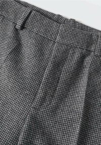 Pantalons à carreaux gris en tissu texturé, dotés d'une taille et de plis, avec un petit détail de passants de ceinture.