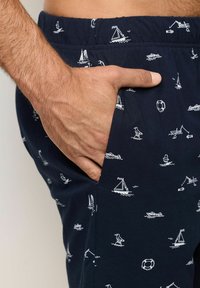 Pantaloni corti navy con stampa bianca a tema nautico, vita elastica, tasche laterali e vestibilità rilassata. Presenta un design con barche e anelli di salvataggio.