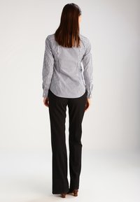 Gestreiftes Hemd in Blau und Weiß, schwarze Schlaghose und High Heels, von hinten betrachtet, zeigt den Stoff und die Passform.