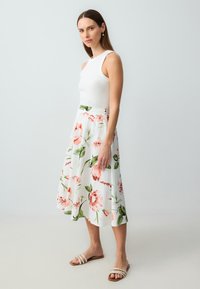 Weißer Rock mit floralem Design in Pink und Grün, kombiniert mit einem enganliegenden weißen Oberteil und hellen Sandalen. Glattes, leichtes Material.