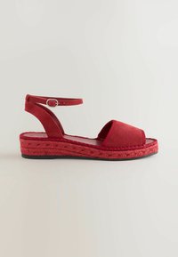 Rød ruskind espadrille sandal med åben tå, ankelrem og vævet jute sål. Har en flad gummibase og syede detaljer.