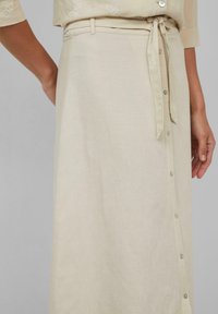 Beige linnen rok met een voorste knoopsluiting, een ceintuur in de taille en een gladde textuur. Beschikt over een zijsleetje en een ingetogen ontwerp.