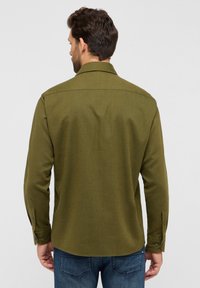 Camicia verde oliva a maniche lunghe con taglio dritto, polsini abbottonati e colletto all'americana. Tessuto strutturato con dettaglio sul retro.