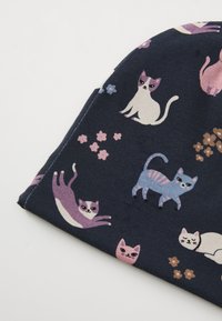 Mütze aus Baumwolle mit einem dunkelblauen Hintergrund und einem Katzenmotiv in verschiedenen Farben, darunter Pink, Weiß und Lila, mit floralen Akzenten.