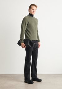 Olijfgroene gebreide trui, zwarte coltrui, zwarte spijkerbroek en zwarte leren oversized clutch. Soepele textuur, aansluitend ontwerp, minimalistische stijl.