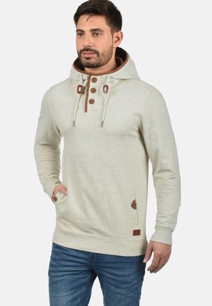 Lichtgrijs hoodie met een gestructureerde afwerking, bruine koorden, knoopaccenten en zijzakken. Draagt men met blauwe spijkerbroeken.
