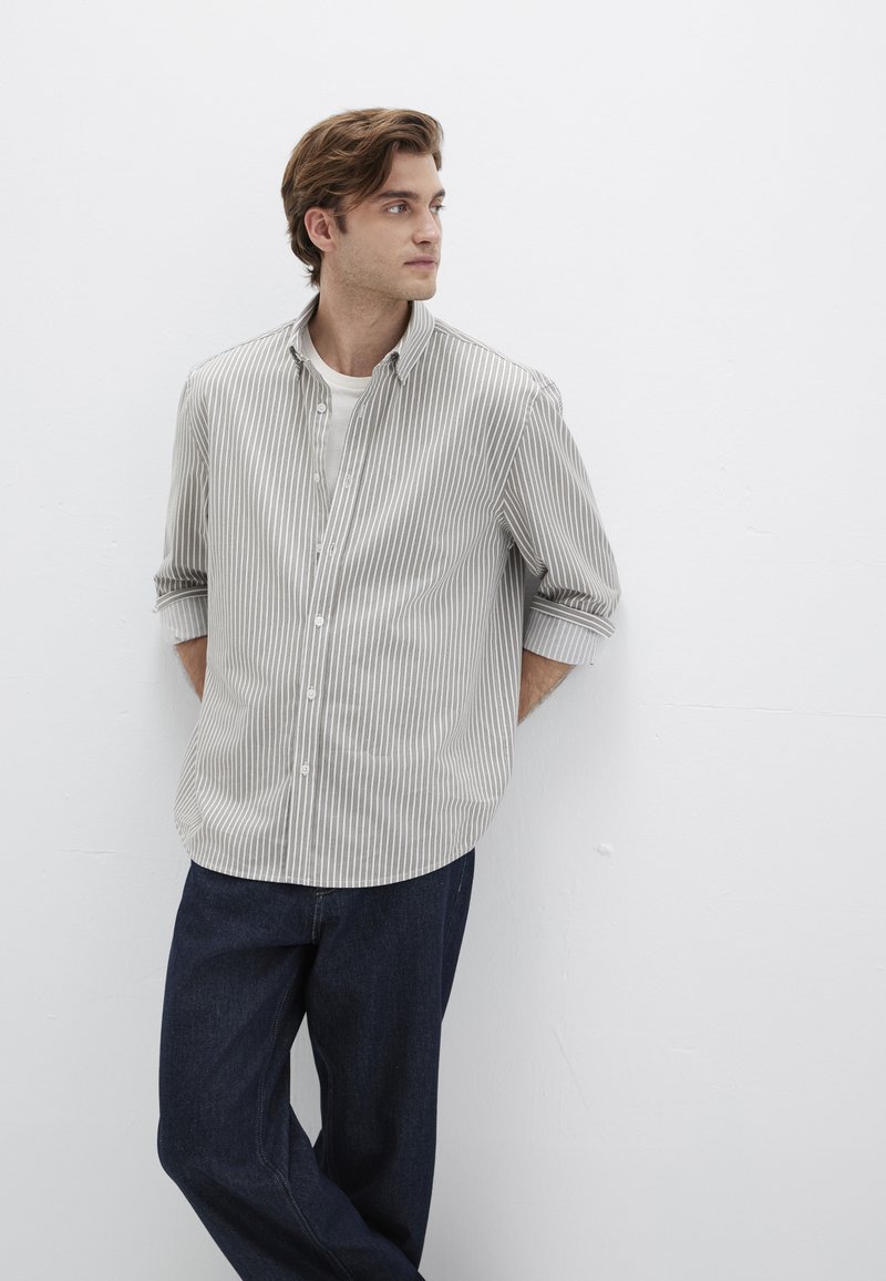 Gestreiftes Hemd mit Knöpfen in Hellgrau und Weiß, lange Ärmel bis zu den Ellbogen hochgekrempelt, kombiniert mit dunklen Jeans. Einfacher Kragen und Knöpfe vorne.