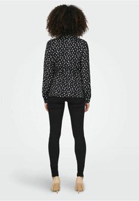 Blusa nera a pois bianchi con maniche lunghe e un design aderente, abbinata a jeans skinny neri e tacchi nudi.