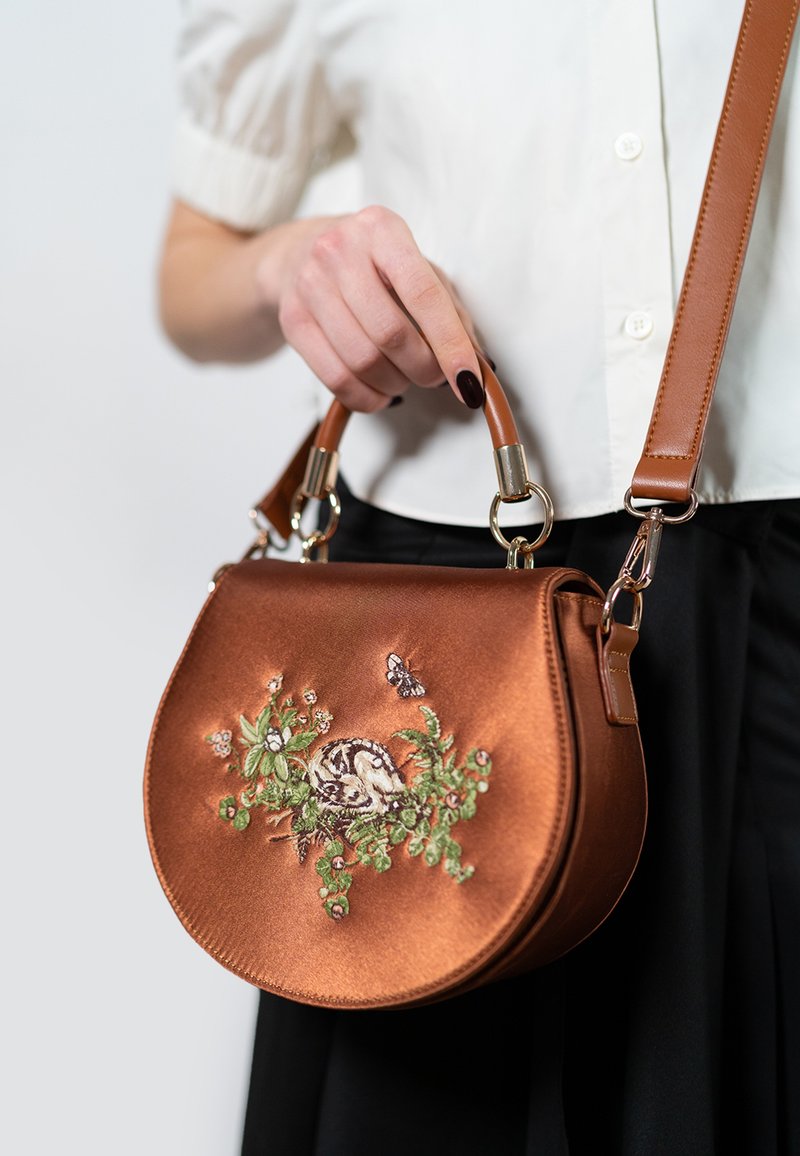 Braune Satin-Handtasche mit aufgesticktem Design, das ein kleines Tier und florale Elemente zeigt. Beinhaltet einen abnehmbaren Schulterriemen und Hardware-Akzente.