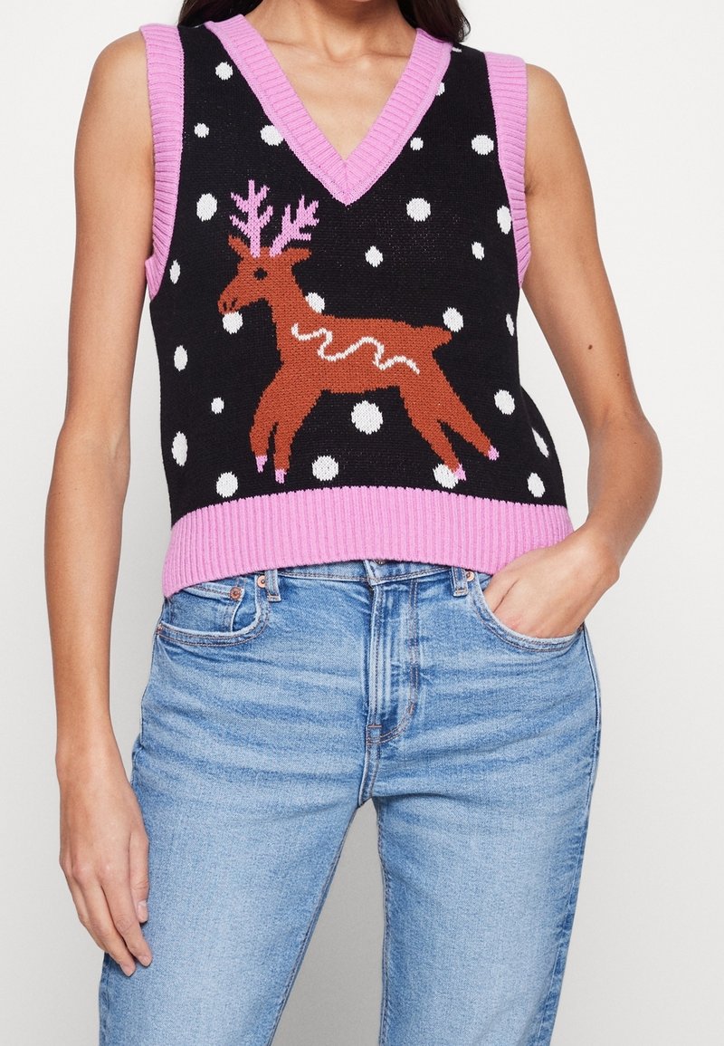 Gilet en tricot noir sans manches avec bordure rose, arborant un renne marron et des flocons de neige blancs, porté avec un jean bleu clair.